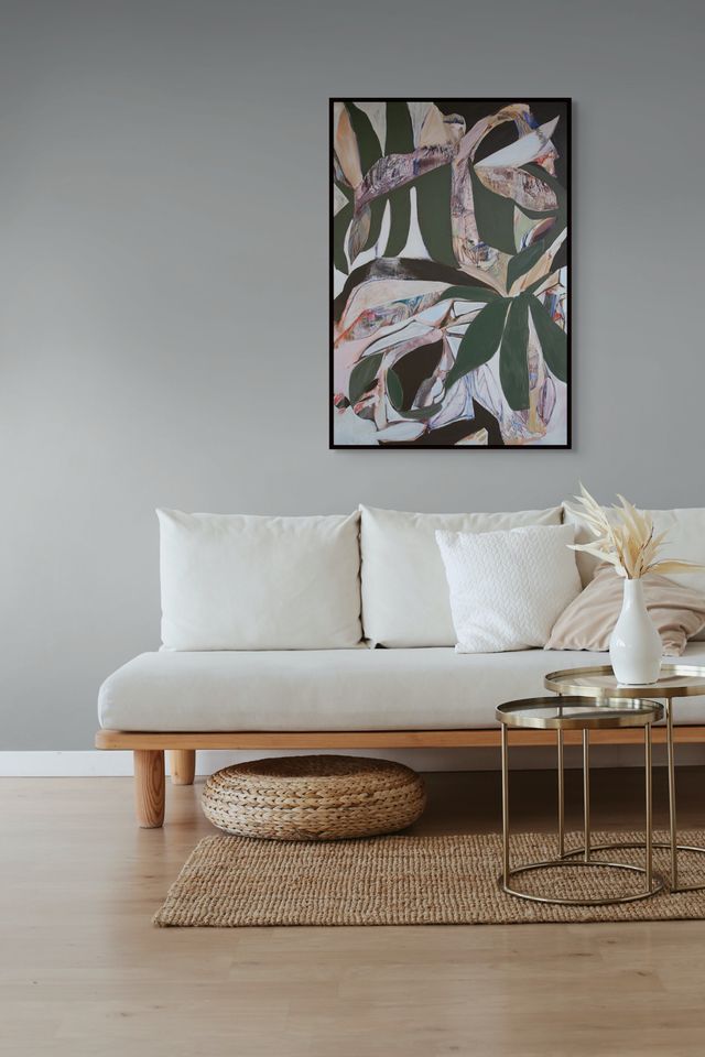 Living room with a beige sofa, decorative pillows, a woven ottoman, and a abstract leaf print painting on the wall.